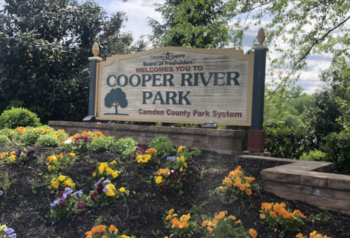 Sign welcoming visitors to Cooper River Park, surrounded by colorful flowers and greenery.