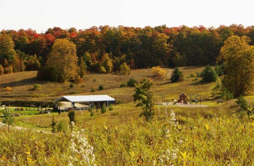A scenic view of a playground surrounded by autumn foliage and grassy fields under a clear sky.