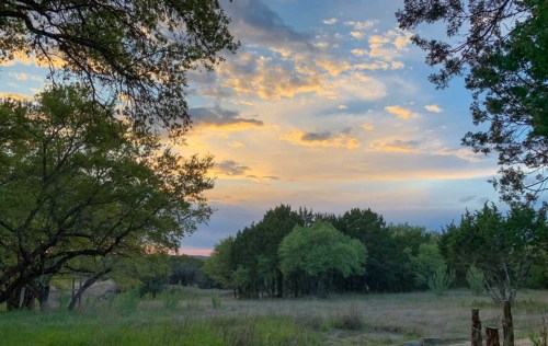 A serene landscape at sunset, featuring trees and a colorful sky with clouds.