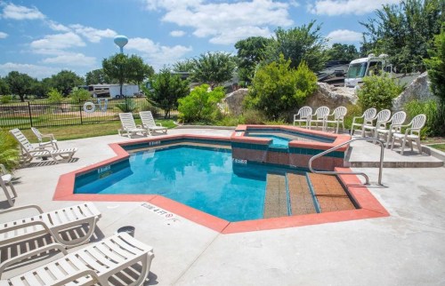 A hexagonal hot tub surrounded by lounge chairs, with a clear blue sky and greenery in the background.
