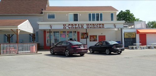 A building labeled "K-Cream Korner" with two parked cars in front and colorful posters on the windows.