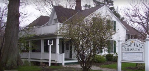 Historic Rose Hill Museum, a white house with green shutters, surrounded by trees and a sign in front.