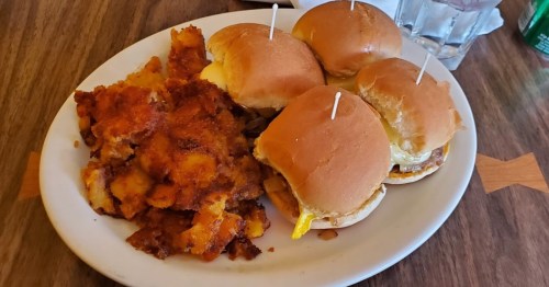 A plate with four sliders and a side of crispy, golden-brown hash browns.