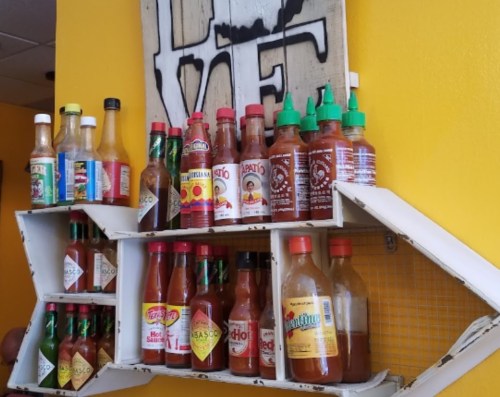 A colorful display of various hot sauce bottles on a wall shelf against a bright yellow background.