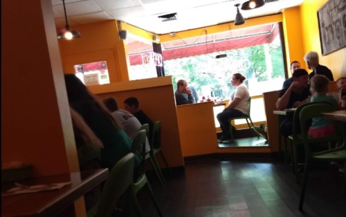A cozy restaurant with bright orange walls, featuring diners at tables and a window view of the outside.