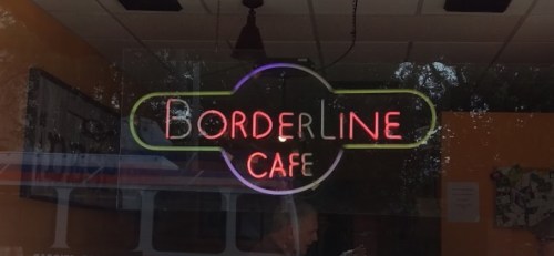 Neon sign for "Borderline Café" displayed in a window, with a colorful, retro design.