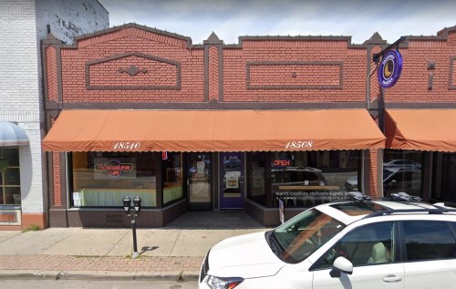 A quaint café with orange awnings and a "Open" sign, located in a brick building on a city street.