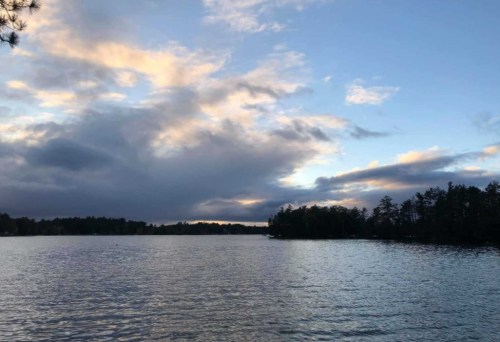 A serene lake scene at dusk, with clouds and a colorful sky reflecting on the water's surface.