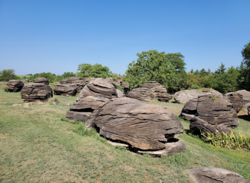 A landscape featuring large, rounded rocks scattered across a grassy area under a clear blue sky.