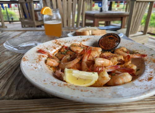 A plate of seasoned shrimp with lemon, served with a drink and bread on a wooden table.