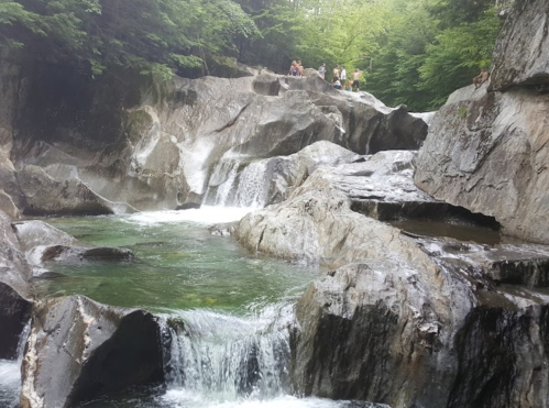 A serene waterfall cascades over rocky terrain, surrounded by lush greenery and visitors enjoying the natural beauty.