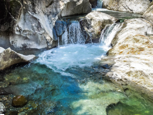 A serene waterfall cascades over rocks into a clear, turquoise pool surrounded by natural stone formations.