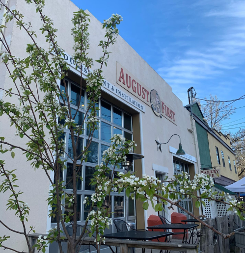 A restaurant named "August First" with a flowering tree in front, set against a clear blue sky.