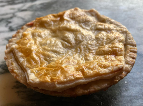 A golden-brown, flaky pastry pie with a slightly wrinkled top crust, resting on a marble surface.