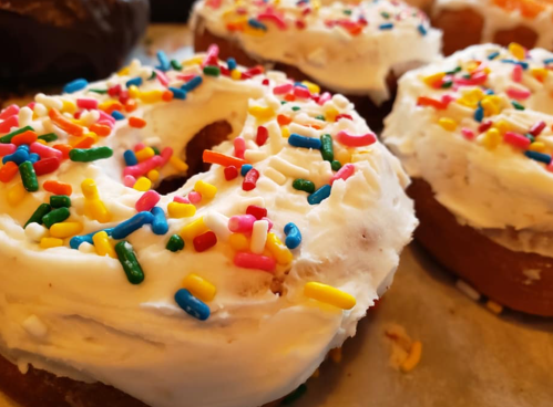 Close-up of frosted donuts topped with colorful sprinkles on a tray.