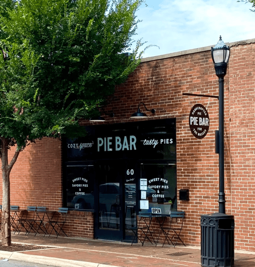 A cozy pie bar with a brick exterior, featuring a sign that reads "Pie Bar" and outdoor seating.