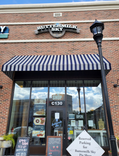 Exterior of Buttermilk Sky shop with a striped awning, open sign, and reserved parking sign in front.