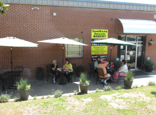 Outdoor seating area of Southern Sweets Bakery, with patrons enjoying food and drinks under umbrellas.