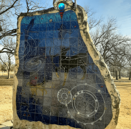 A large, colorful mosaic mural featuring celestial designs and deer, set in a grassy outdoor area.