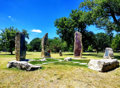 A circle of tall, colorful stone sculptures in a grassy park under a clear blue sky.