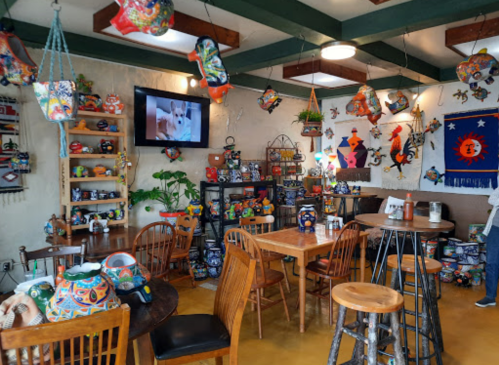 Colorful decor fills a cozy restaurant, featuring painted pottery, wooden tables, and a TV displaying a video.