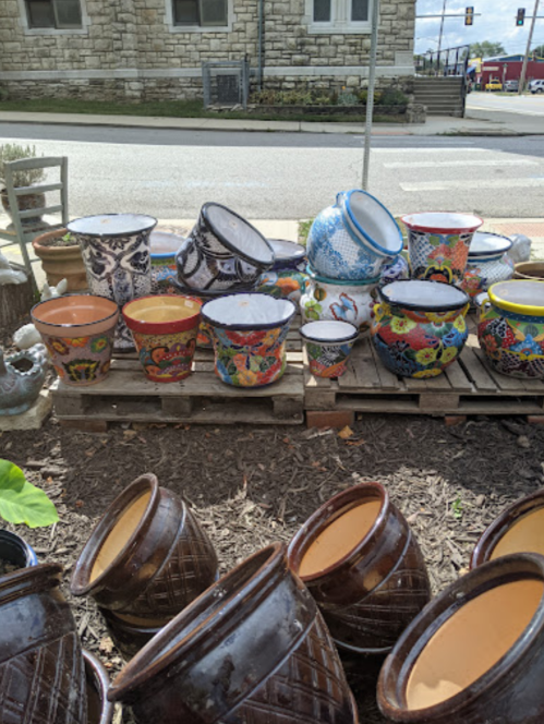 A variety of colorful decorative pots and planters displayed on wooden pallets outdoors.