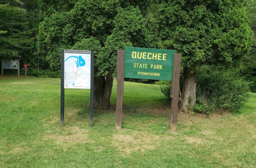 Sign for Quechee State Park with a map and picnic area, surrounded by greenery.
