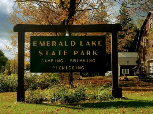Sign for Emerald Lake State Park, listing activities: camping, swimming, and picnicking, surrounded by autumn foliage.