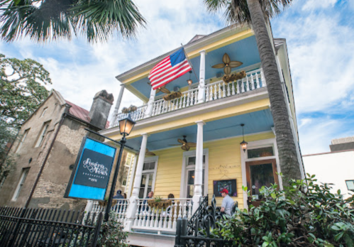 A charming yellow house with an American flag, featuring a porch and palm trees, set in a lively neighborhood.