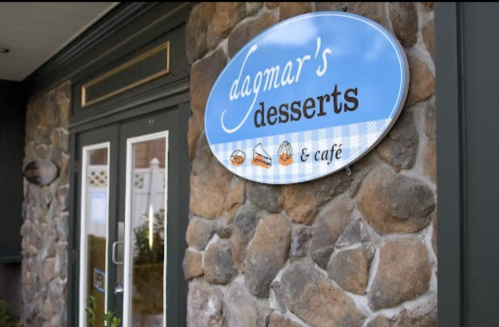 Sign for "Dagmar's Desserts & Café" on a stone wall, featuring a blue background with dessert icons.