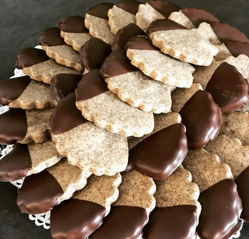 A close-up of a plate stacked with cookies, half-dipped in chocolate, arranged in a decorative pattern.