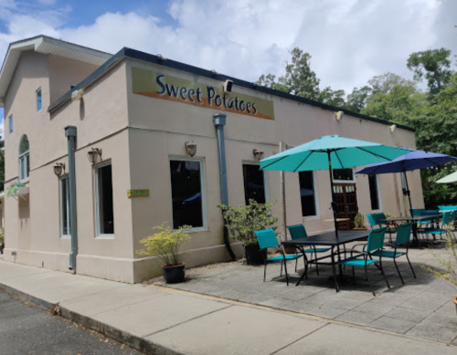 Exterior of a restaurant named "Sweet Potatoes," featuring outdoor seating with umbrellas on a sunny day.
