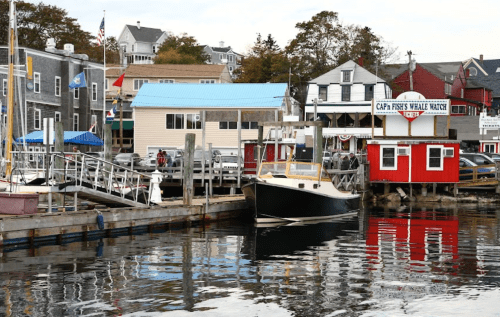 A harbor scene with boats, colorful buildings, and reflections on the water, showcasing a coastal town atmosphere.