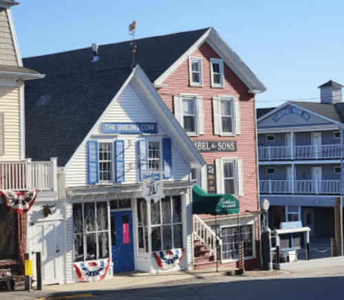 Colorful buildings in a coastal town, featuring shops and a hotel, with decorative bunting and clear blue skies.