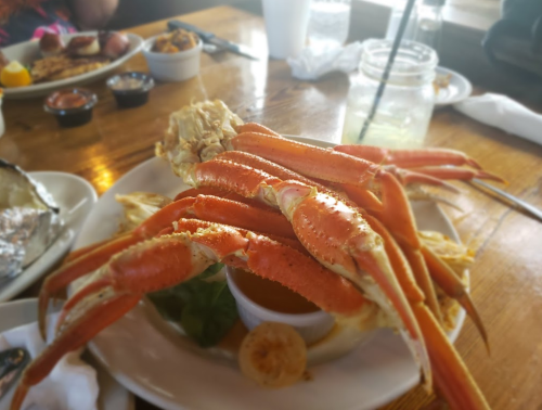 A plate of crab legs with a small bowl of dipping sauce, surrounded by side dishes on a wooden table.