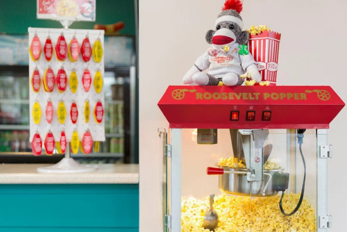 A popcorn machine with a stuffed monkey on top, next to a display of colorful tags and a popcorn bucket.