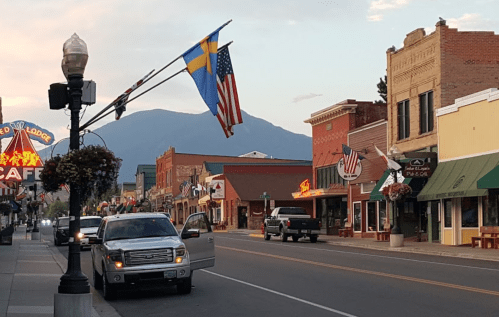 A charming small town street with flags, shops, and mountains in the background during sunset.