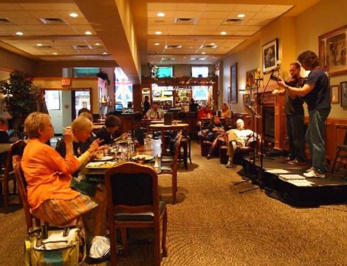 A lively restaurant scene with musicians performing on stage while diners enjoy their meals at tables.
