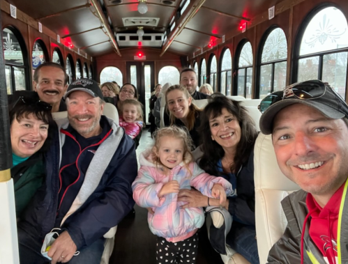 A group of smiling people, including adults and children, posing together inside a trolley bus.