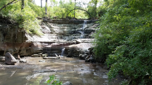 A serene waterfall cascading over rocky cliffs, surrounded by lush green foliage and a calm pool below.