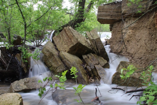 A serene scene of flowing water cascading over rocks, surrounded by lush green foliage and trees.