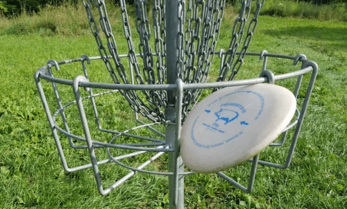 A close-up of a disc golf basket with a disc resting on the edge, set in a grassy field.