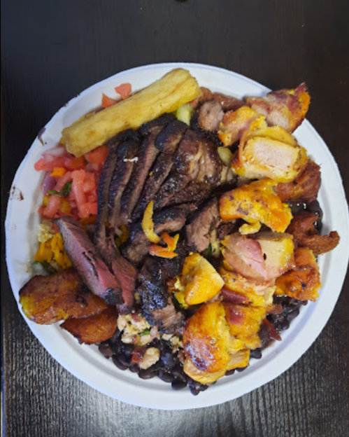 A colorful plate of grilled meats, fried plantains, rice, black beans, and fresh tomatoes.