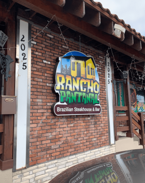 Sign for "Rancho Pantanal," a Brazilian steakhouse and bar, displayed on a brick wall with a colorful design.