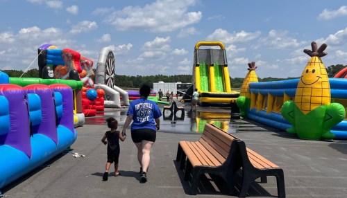 A child and adult walk towards colorful inflatable attractions at an outdoor event on a sunny day.