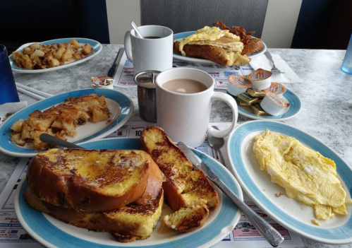 A breakfast spread featuring French toast, an omelet, hash browns, coffee, and creamers on a table.