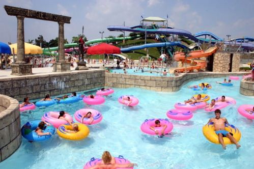 A busy water park with colorful inner tubes floating in a lazy river, surrounded by slides and sunbathers.