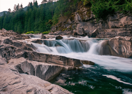 A serene river flows over smooth rocks, surrounded by lush green trees and a tranquil forest landscape.