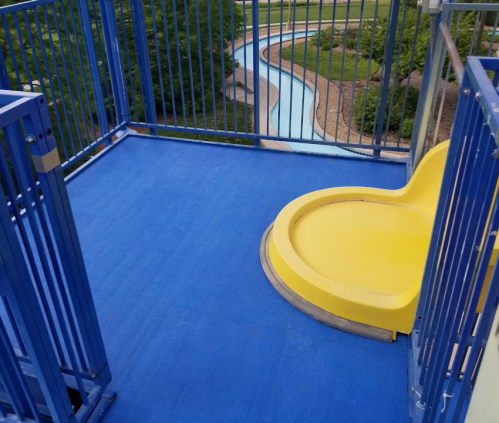 A bright yellow water slide entrance on a blue platform, overlooking a winding waterway in a park.