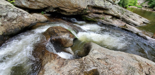 A rocky riverbed with flowing water cascading over smooth stones and through natural formations.